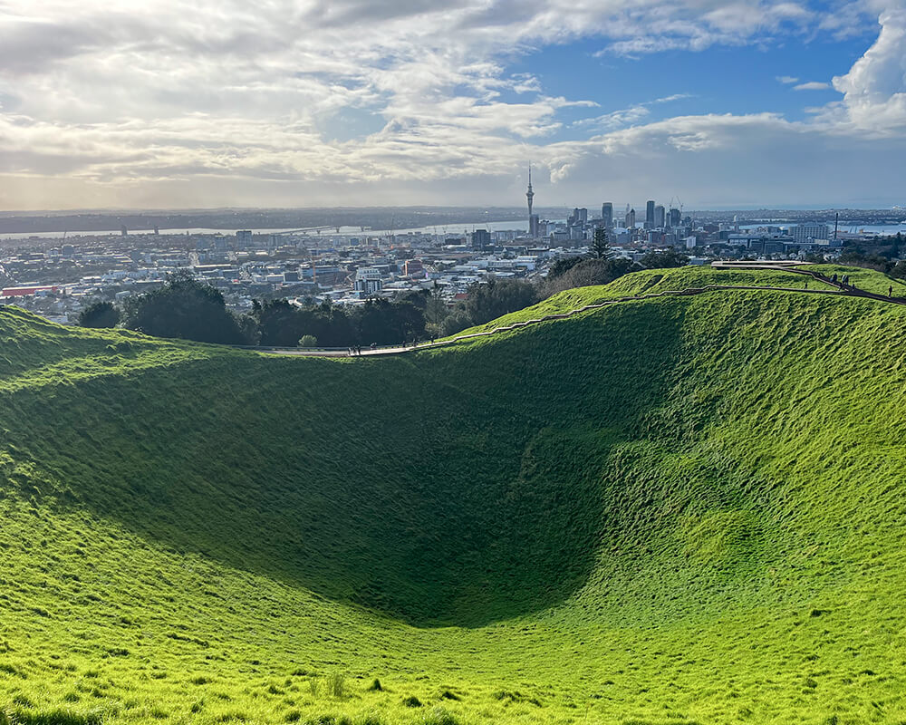 mit Gras bewachsener Krater, im Hintergrund die Skyline von Auckland