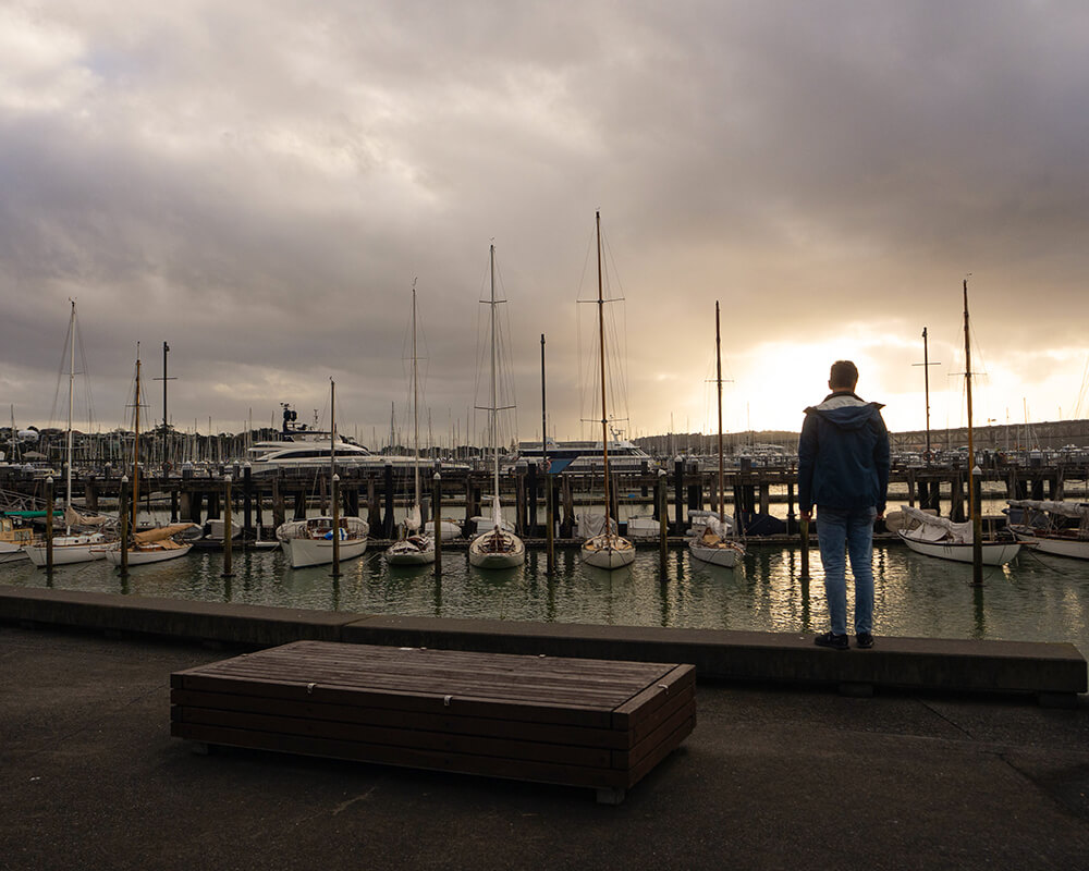 Mann steht vor einem Hafen voller Segelboote während des Sonnenuntergangs