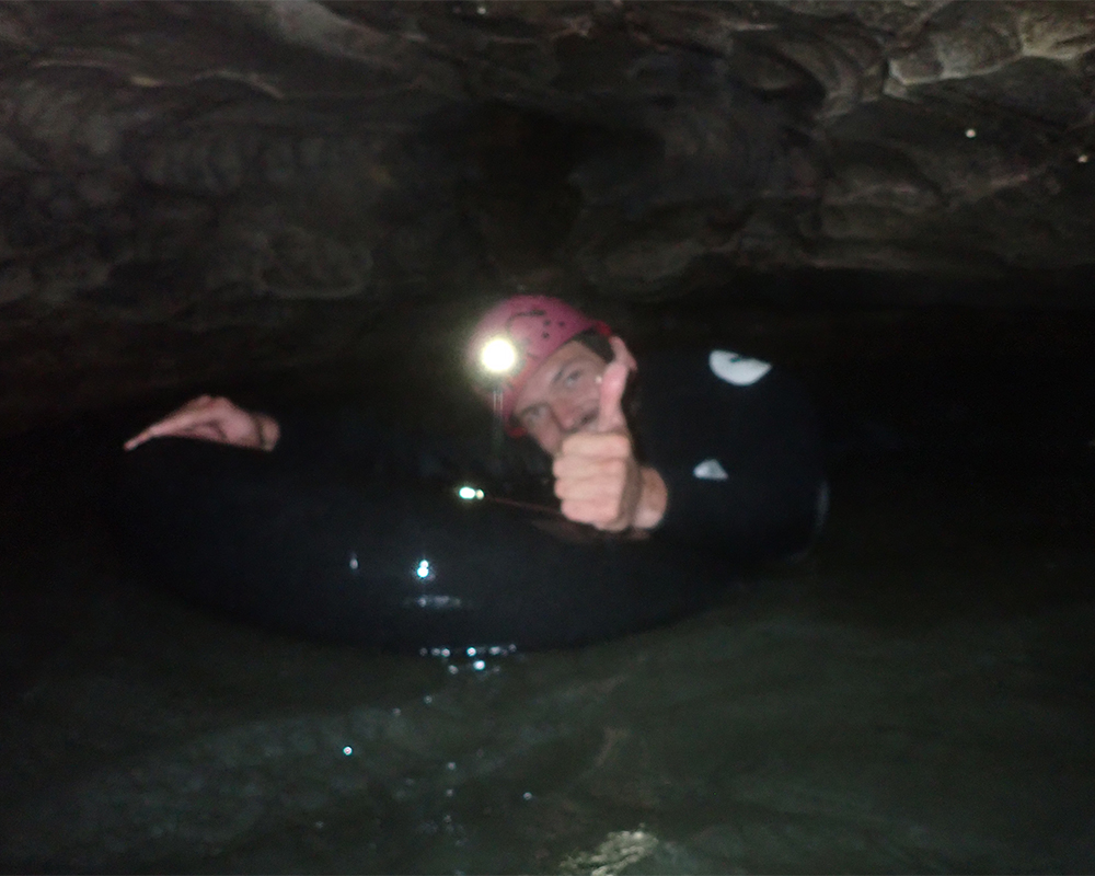 Mann hält sich an einem Reifen fest, schwimmt durchs Easser, über ihm Felsen