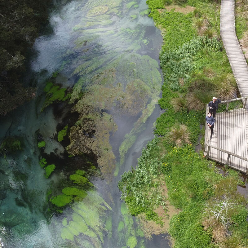 Blauer Fluss mit Moos, junges Paar steht rechts auf einer Holzplattform