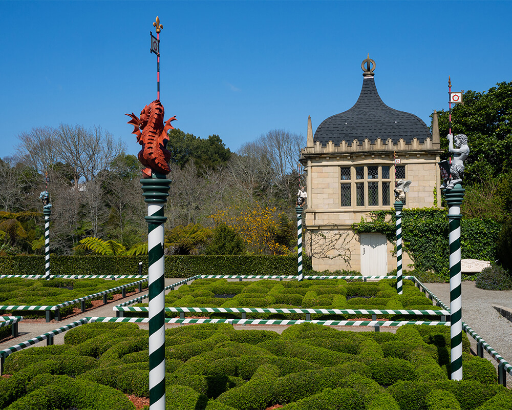 Garten mit Büschen, einem Gebäude im Hintergrund und mittelalterlichen Säulen