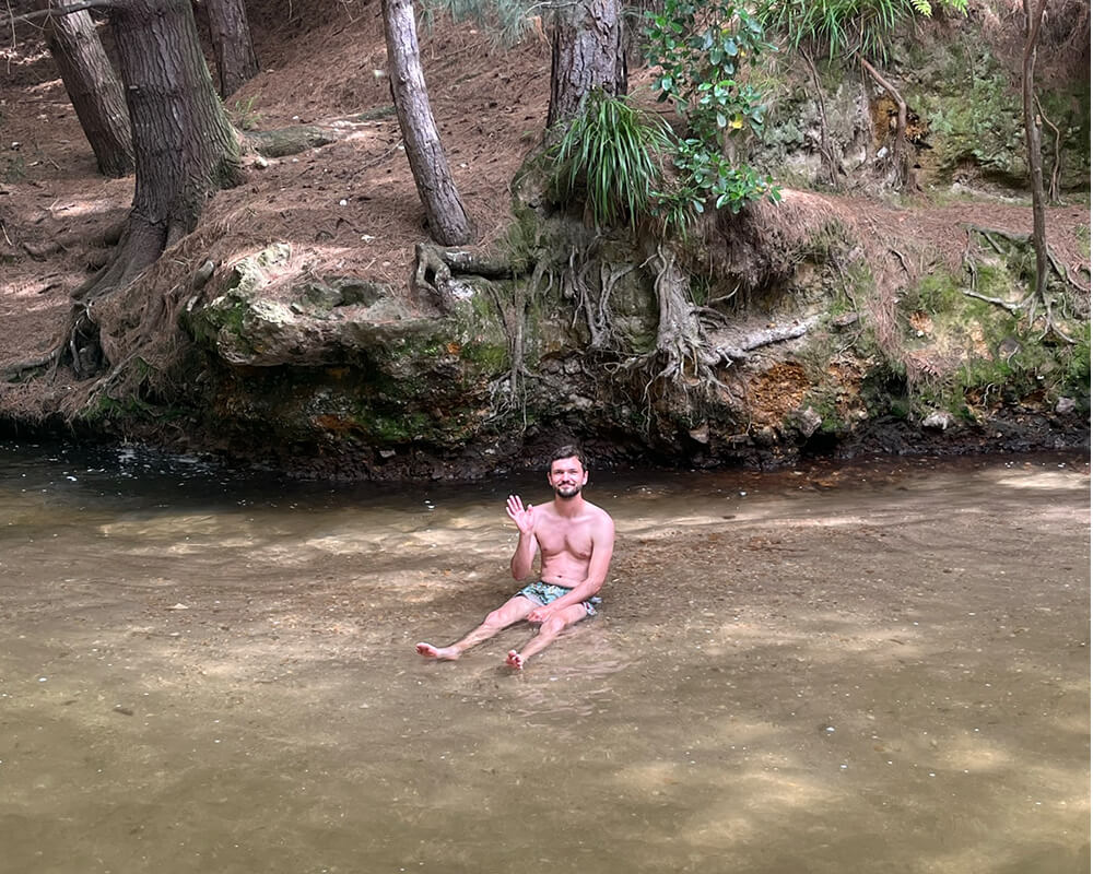 junger Mann sitzt in einem flachen Fluss im Wald