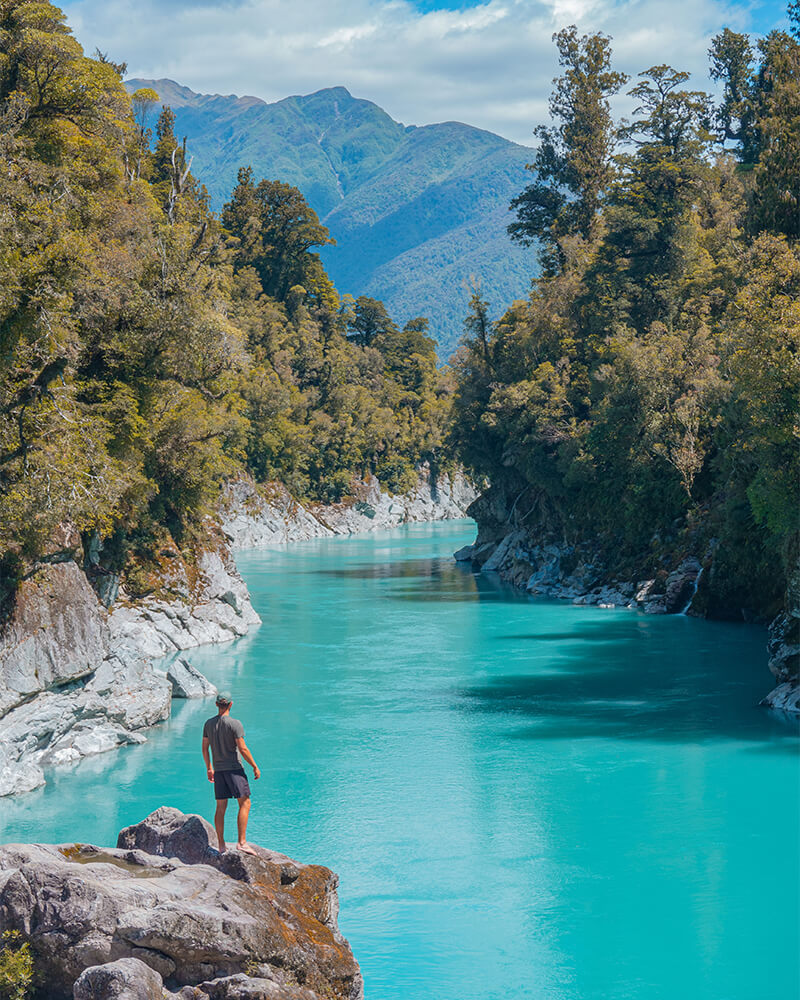 junger an steht auf einem Felsen an dem türkisenen Fluss des Hokitika Gorge